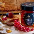 a jar of honey next to a piece of bread with berries and nuts