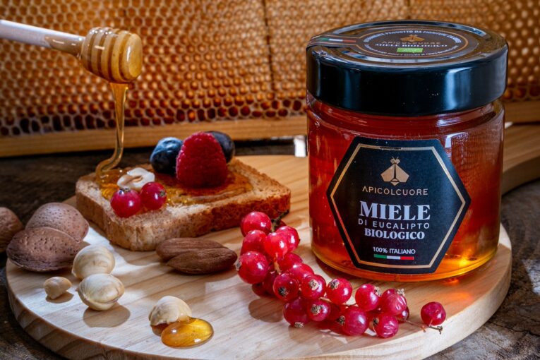 a jar of honey next to a piece of bread with berries and nuts